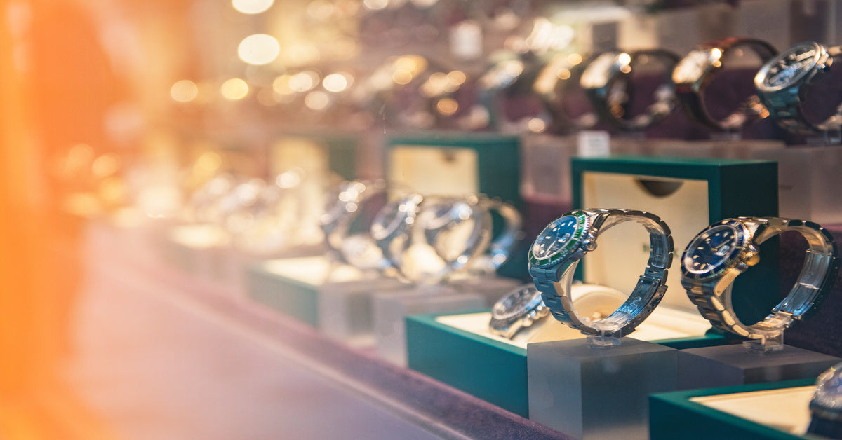 Side view at an angle of luxury watches in a display case. Some are shown in their open boxes; others are on stands.