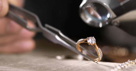 Tweezers hold a ring under a magnifying loupe. The gold ring has a round center diamond and small accent diamonds.