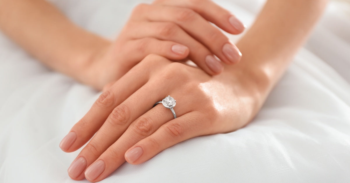A close-up view shows a person wearing a white dress, placing their hands gently in their lap and wearing a diamond ring.