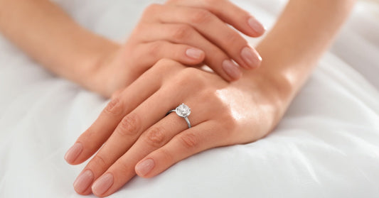 A close-up view shows a person wearing a white dress, placing their hands gently in their lap and wearing a diamond ring.