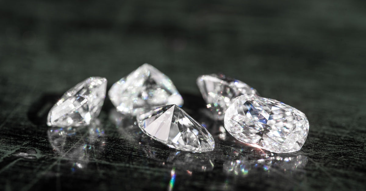 A close-up of a group of five round-cut diamonds sparkling brightly on a scratched black surface.