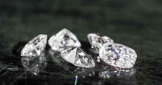 A close-up of a group of five round-cut diamonds sparkling brightly on a scratched black surface.