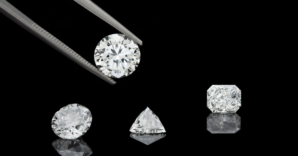 Various diamond cuts on a black background, including round, emerald, and brilliant. Tweezers hold up a round diamond.